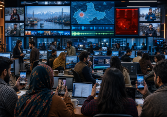 Newsroom staff monitor live broadcasts, maps, audio feeds, and video editing screens in a busy control room